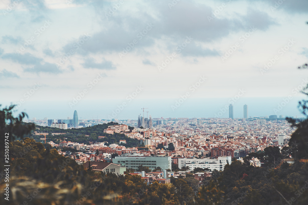 Beautiful scenery of a sunset in Barcelona, Spain: the cityscape with Sagrada Familia and many other famous buildings, different districts and houses, the sea in the distance, hills and greenery