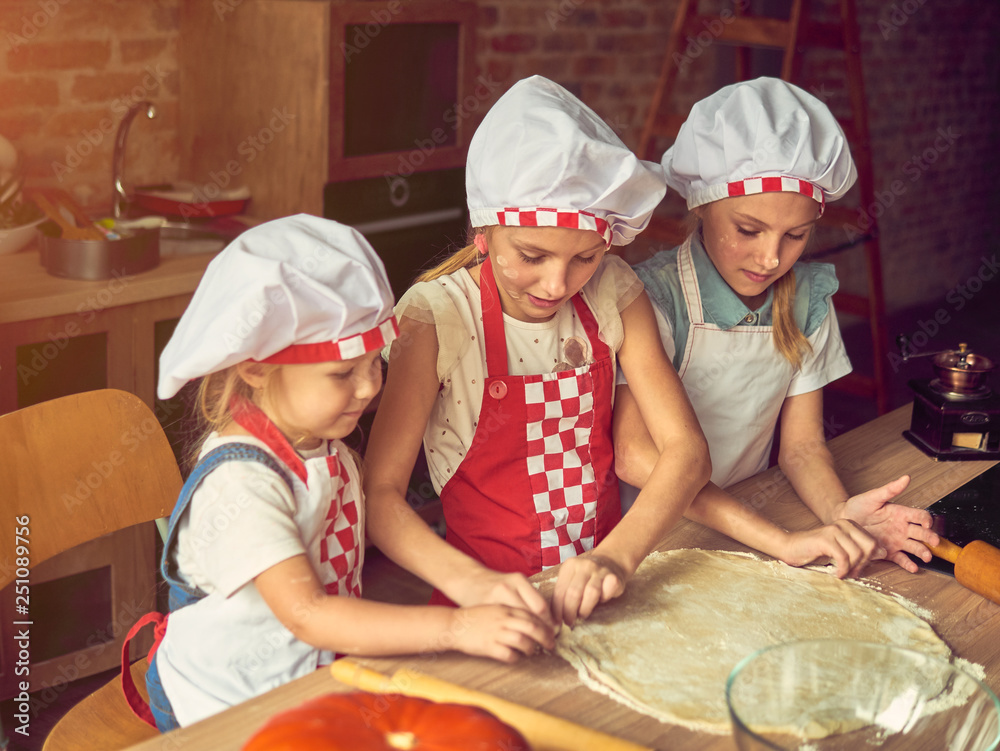 Cute little girls are smiling while cooking in kitchen at home Cute little girls are smiling while cooking in kitchen at home