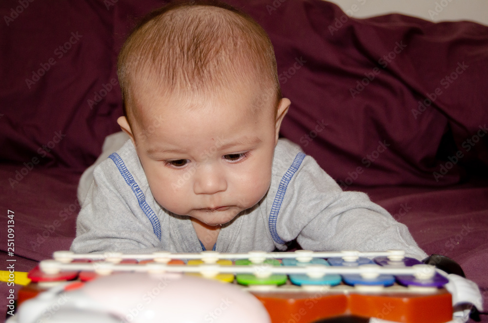 cute 4 months old baby boy having tummy time and looking into colorful xylophone cute 4 months old baby boy having tummy time and looking into colorful xylophone