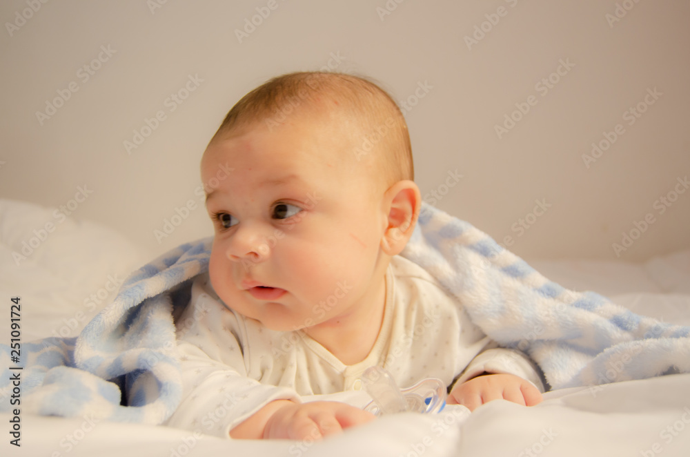 cute 4 months old baby boy having tummy time on white quilt covered with blue blanket