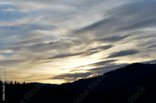 Cloudy dramatic sky over silhouette landscape during winter at sunset