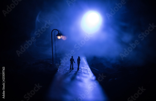 Young couple holding each other hands. Slowly walking under white street lights in night. Dark time. Peaceful atmosphere in mist. Foggy air.