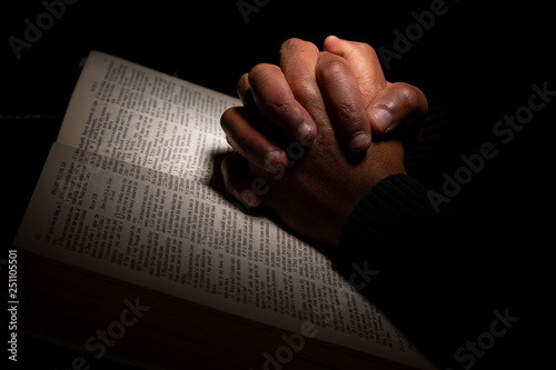 African American Man Praying with Hands on Top of the Bible.