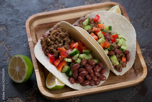 Mexican tacos with minced beef meat, red beans and fresh vegetables filling on a wooden serving tray