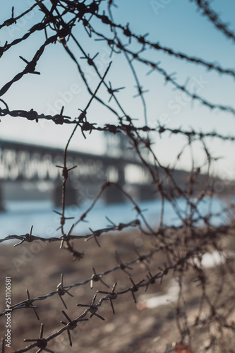 Automobile and railroad bridge behind barbed wire. Barbed Wire Fence and Bridge. Barb wire close up. Blur bridge behind barb wire.