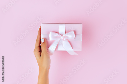 Fototapeta Naklejka Na Ścianę i Meble -  Woman hands holding present box with pink bow on pastel pink background. Flat lay style.