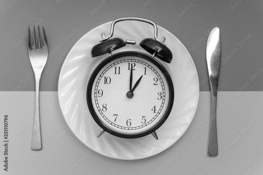 Alarm clock with fork and knife on the table. Time to eat, Breakfast, Lunch time and dinner concept. Black and White Concept Alarm clock with fork and knife on the table. Time to eat, Breakfast, Lunch time and dinner concept. Black and White Concept