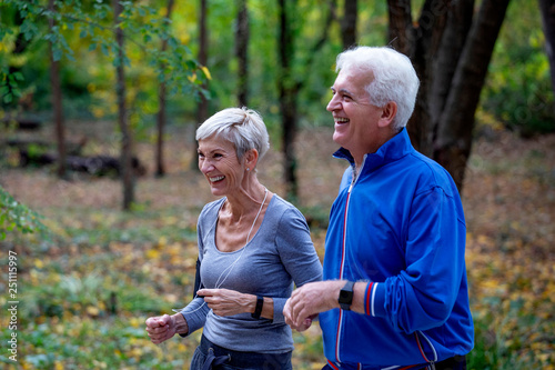 Active senior couple jogging in the park at autumng day and smile