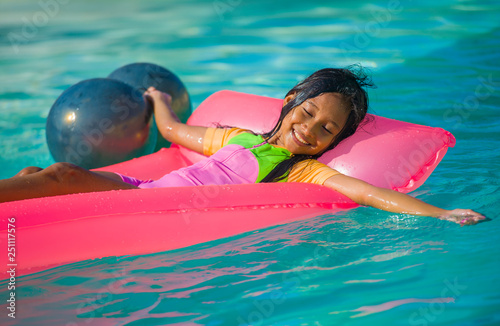 lifestyle outdoors portrait of young happy and cute female child having fun with inflatable airbed in holidays resort swimming pool smiling carefree and cheerful