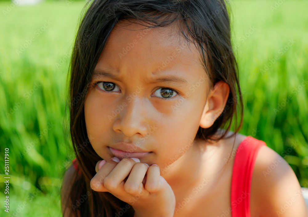 outdoors portrait of beautiful and sweet 8 years old young girl looking with intense gorgeous eyes to the camera, the child  in a red dress isolated on a green field
