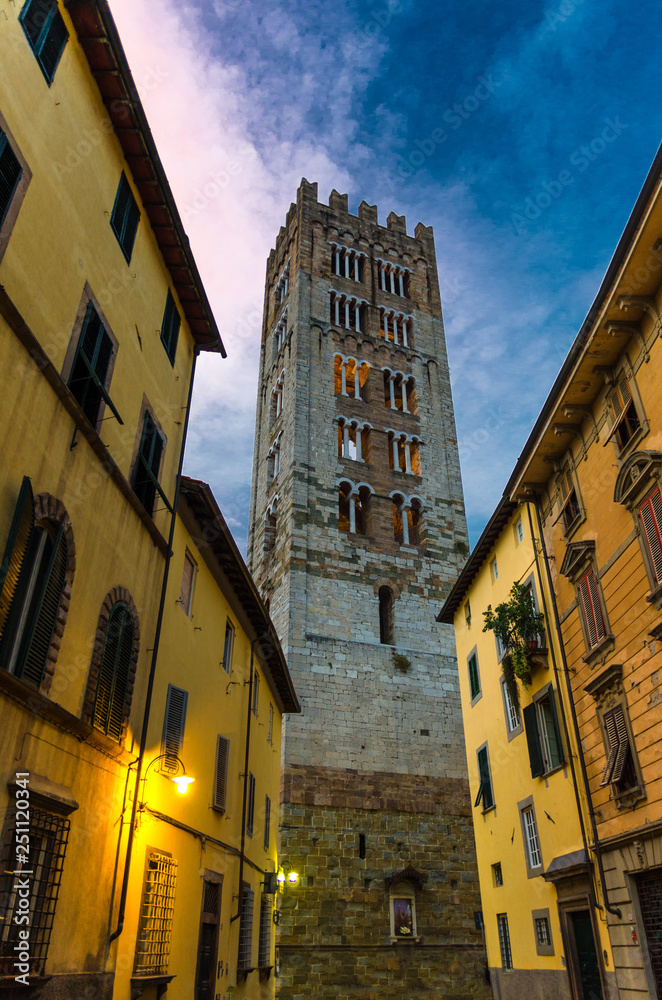 Bell tower of Chiesa di San Frediano catholic church view through narrow street with lamp light in historical centre of old medieval town Lucca, evening view, Tuscany, Italy