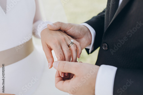 the bride in a white dress and the groom in a suit put the wedding ring on each other