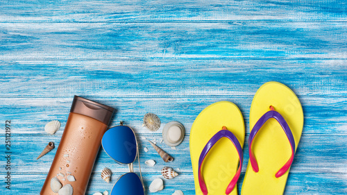 Bright yellow flip flops with sunglasses and sunscreen as concept of vacation time on blue background