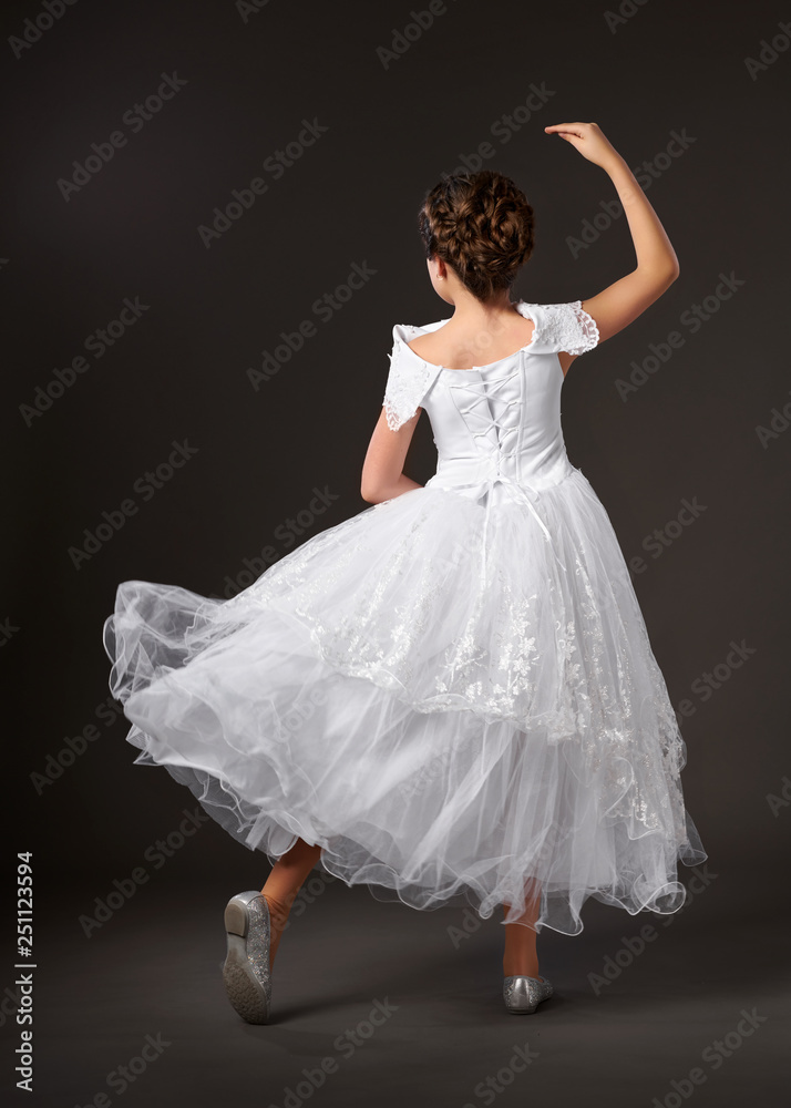 Fototapeta premium little girl is dancing in a white ball gown, dark background