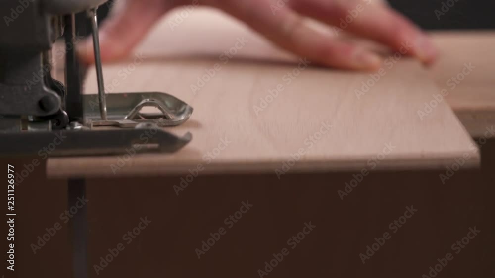 A side view of a power jigsaw cutting a piece of wooden board A side view of a power jigsaw cutting a piece of wooden board