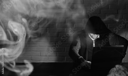 Hacker in black mask and hood at the table