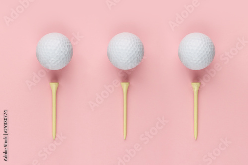 Three golf ball and wooden tee on pink background closeup