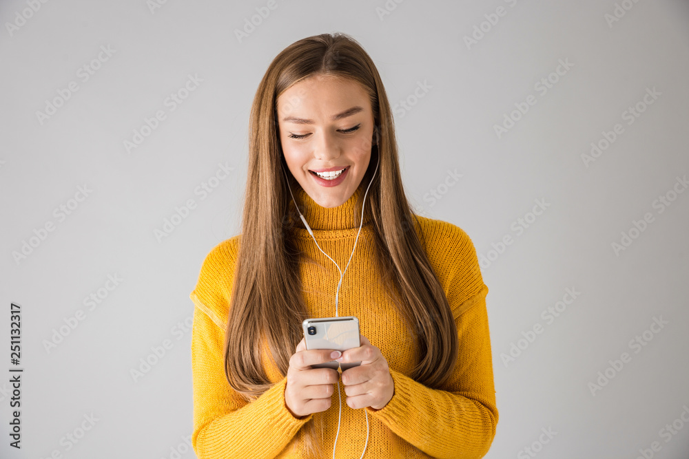 Happy young woman isolated over grey wall background using mobile phone.