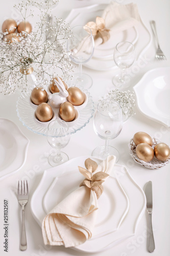 Happy Easter! Golden decor and table setting of the Easter table with white dishes of white color. © COLOR PHOTO