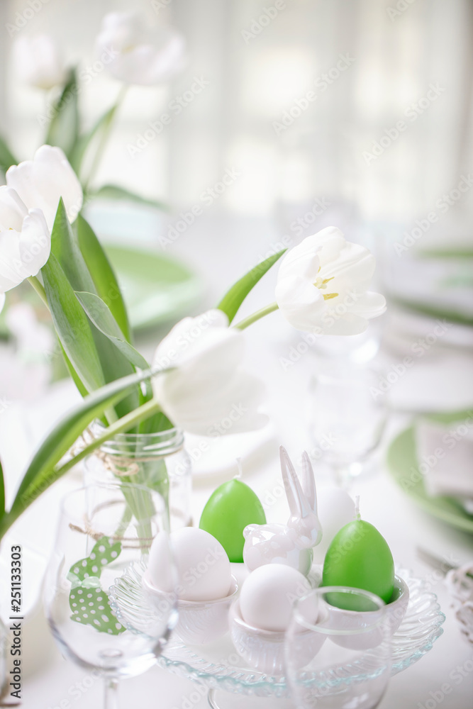 Decor and table setting of the Easter table with white tulips and dishes of green and white color. Easter decor in the form of Easter bunnies  green color with white polka dots.