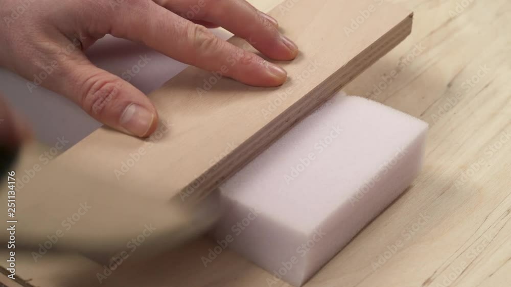 A side view of man's hand holding knife and cutting off a piece of furniture poly foam A side view of man's hand holding knife and cutting off a piece of furniture poly foam