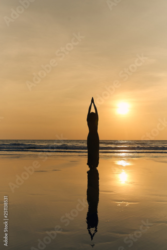 Woman dressed in a beautiful long dress and doing yoga at sunset on the beach. Female performing asanas and enjoying life on the sea