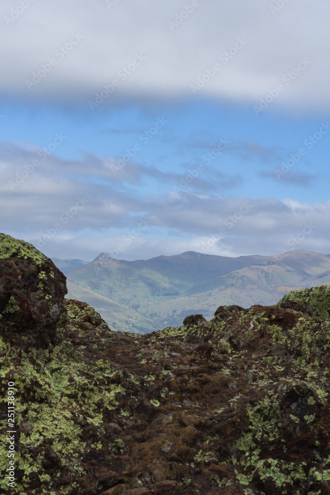 Dark rocks and mountain peak in distance with dramatic sky during sunny day