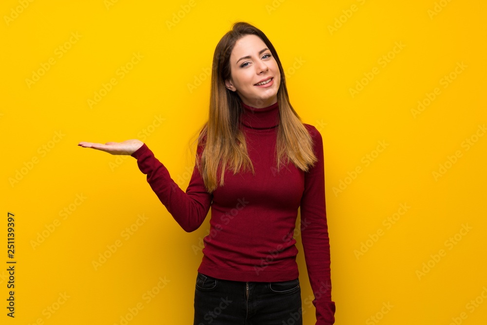 Woman with turtleneck over yellow wall holding copyspace imaginary on the palm to insert an ad Woman with turtleneck over yellow wall holding copyspace imaginary on the palm to insert an ad