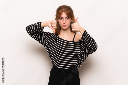 Young redhead woman over white wall making good-bad sign. Undecided between yes or not © luismolinero