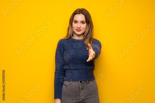 Teenager girl over yellow wall shaking hands for closing a good deal