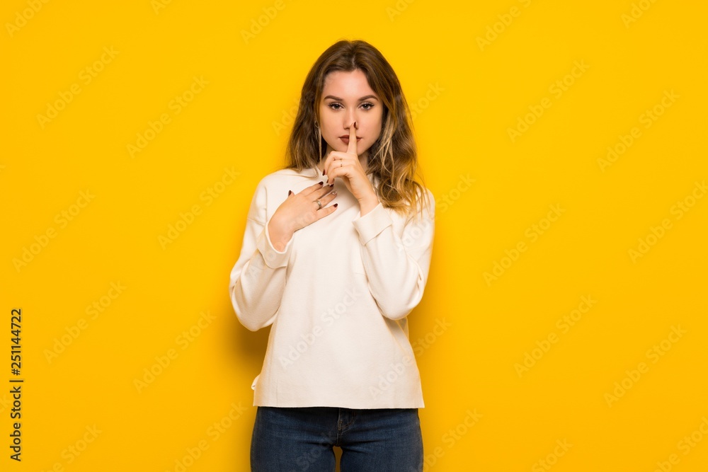Teenager girl over yellow wall showing a sign of silence gesture putting finger in mouth Teenager girl over yellow wall showing a sign of silence gesture putting finger in mouth