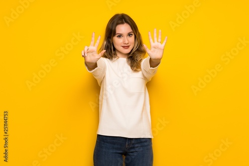 Teenager girl over yellow wall counting eight with fingers