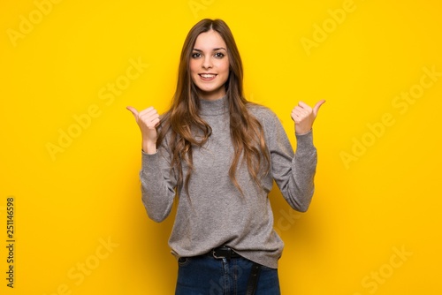 Young woman over yellow wall giving a thumbs up gesture with both hands and smiling