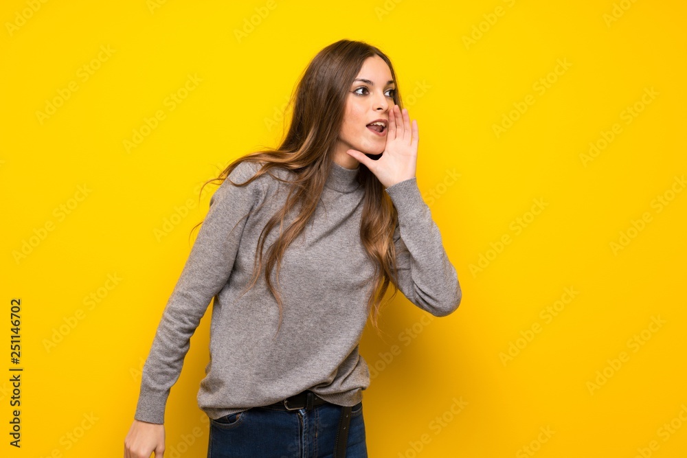 Young woman over yellow wall shouting with mouth wide open to the lateral Young woman over yellow wall shouting with mouth wide open to the lateral