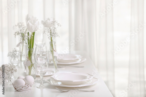 Happy Easter! Decor and table setting of the Easter table with white tulips and dishes of white color.