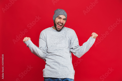 Image of positive man 30s with beard and mustache shouting and rejoicing while standing, isolated over red background