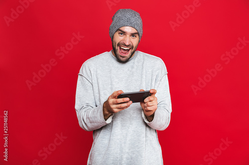 Image of optimistic man 30s holding smartphone and playing video games, isolated over red background © Drobot Dean