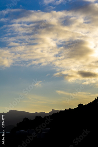 White clouds over mountains peaks, dramatic sunset with black foreground 