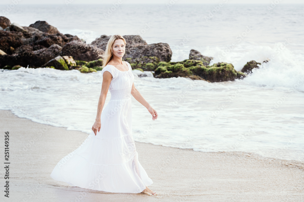 Attractive happy mature tourist blonde woman in long white dress on asian sand tropical beach. Attractive happy mature tourist blonde woman in long white dress on asian sand tropical beach.