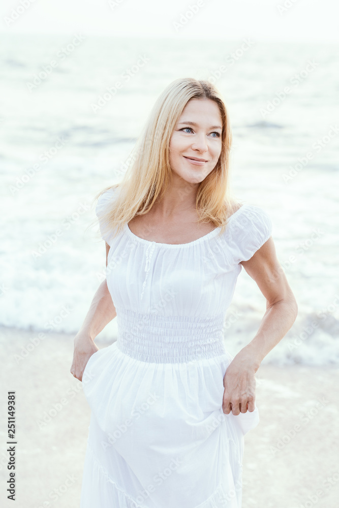 Attractive happy mature tourist blonde woman in long white dress on asian sand tropical beach. Attractive happy mature tourist blonde woman in long white dress on asian sand tropical beach.