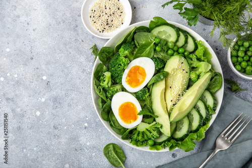 healthy green salad with avocado, eeg, broccoli, cucumber, green peas and spinach in white  bowl