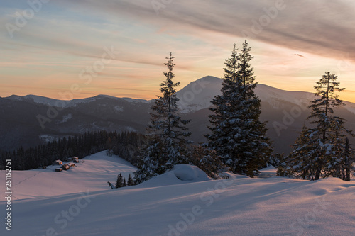 Dramatic wintry scene with snowy house. Fantastic colors of the sunset in the winter Carpathians with the shepherds' hut in the foreground and high peaks on the horizon