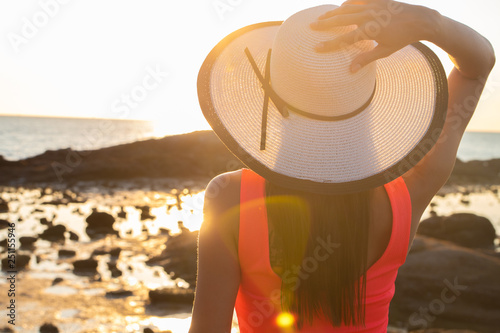 girl in a hat strolls along the beach at sunset