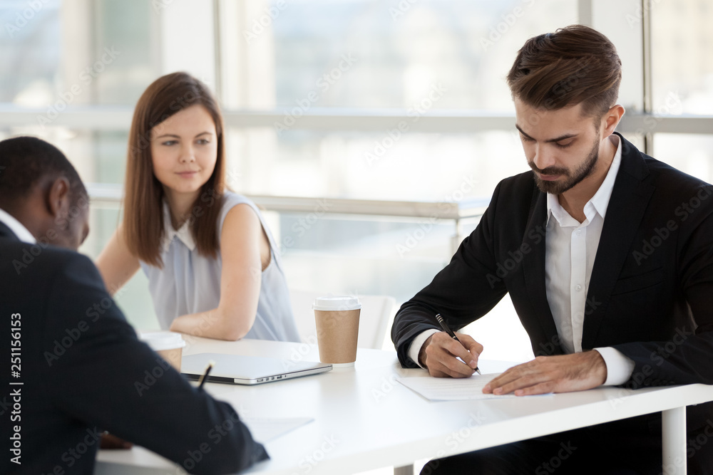 Diverse business colleagues signing agreement sitting at desk Diverse business colleagues signing agreement sitting at desk