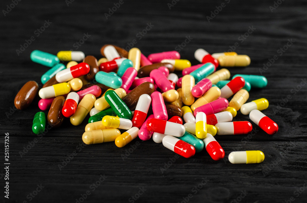 A lot of colorful pills capsules pills in a pile on a wooden table black