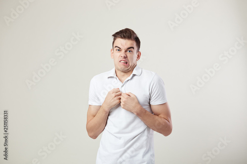 Surprised guy dressed in a white t-shirt and jeans feels disgusting on a white background in the studio