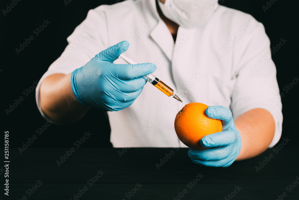 Orange injection, lab technician in Bathrobe and gloves colitis nitrates and GMO in Orange on black background Orange injection, lab technician in Bathrobe and gloves colitis nitrates and GMO in Orange on black background