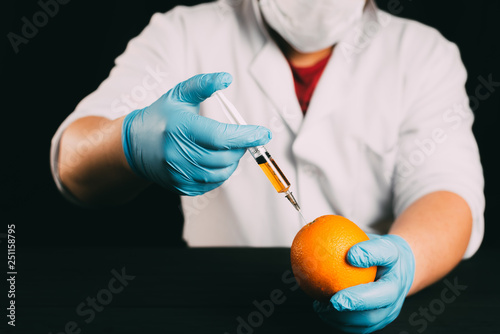 Orange injection, lab technician in Bathrobe and gloves colitis nitrates and GMO in Orange on black background photo