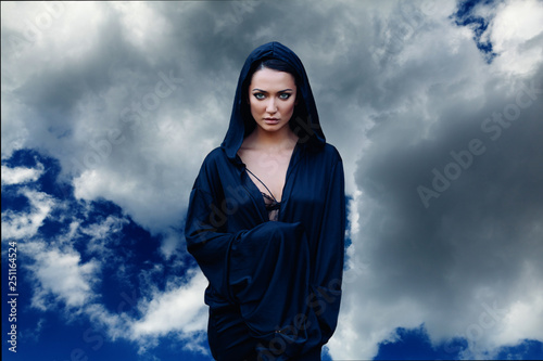 Obraz na plátně Young beautiful woman with black hair and in the dark blue cloak with hood at th