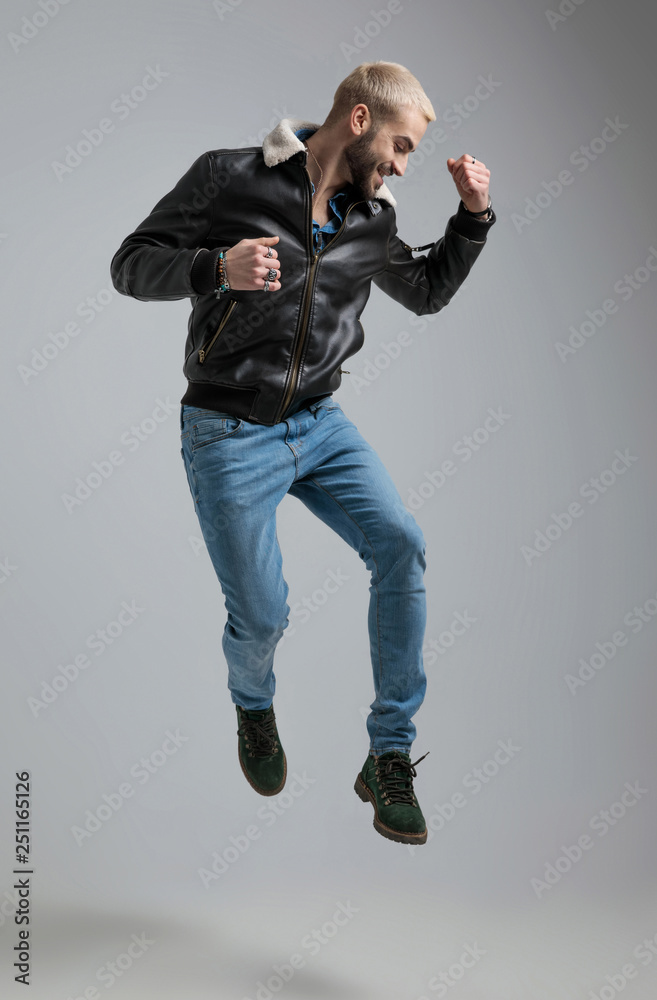 man in leather jacket and jeans jumps and raises fist into the air